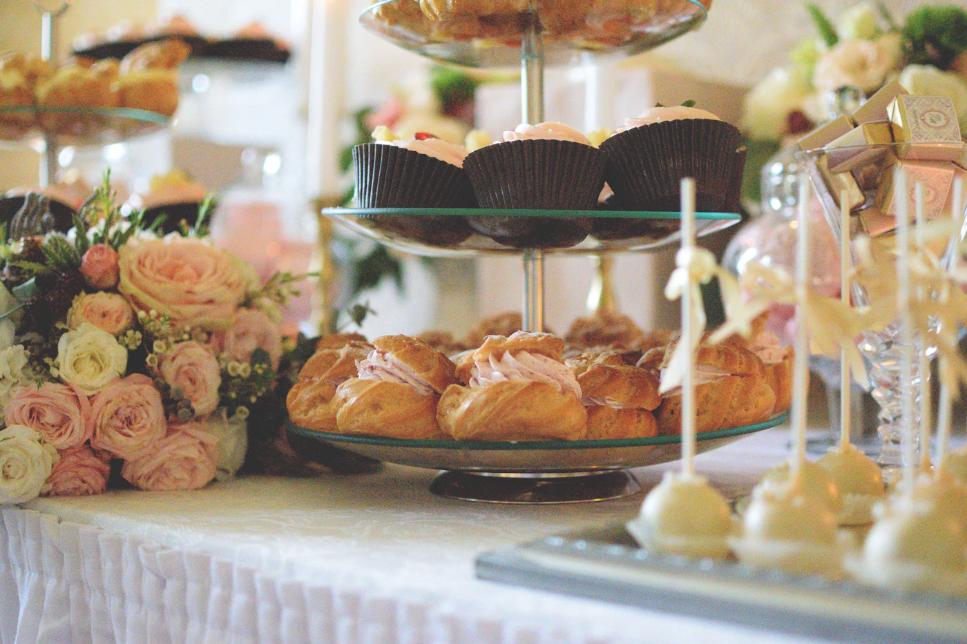 Masă de candy bar cu etajere de cupcakes, eclere și flori.